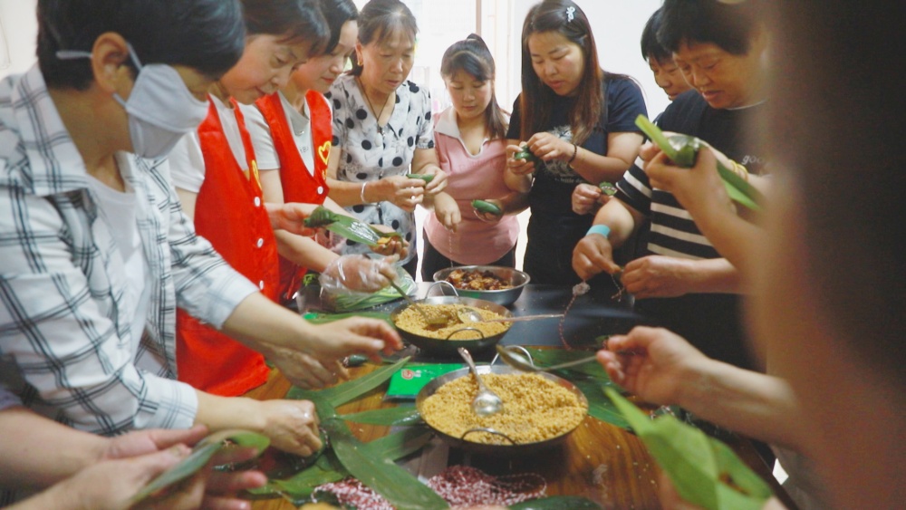 圖為社區(qū)工作人員及社區(qū)居民共同手工包粽子.jpg